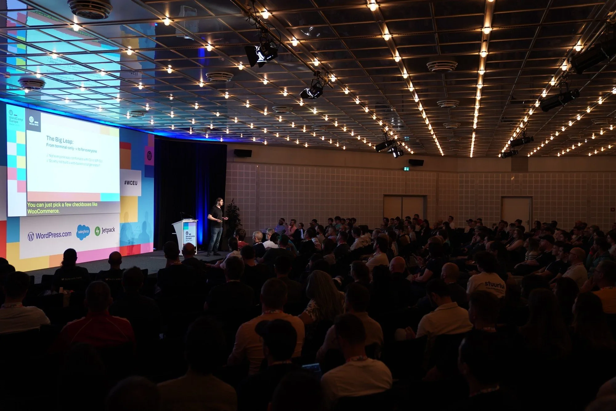 Marcel Tannich on stage at WordCamp Europe 2025 in Basel, seen from the back of the room